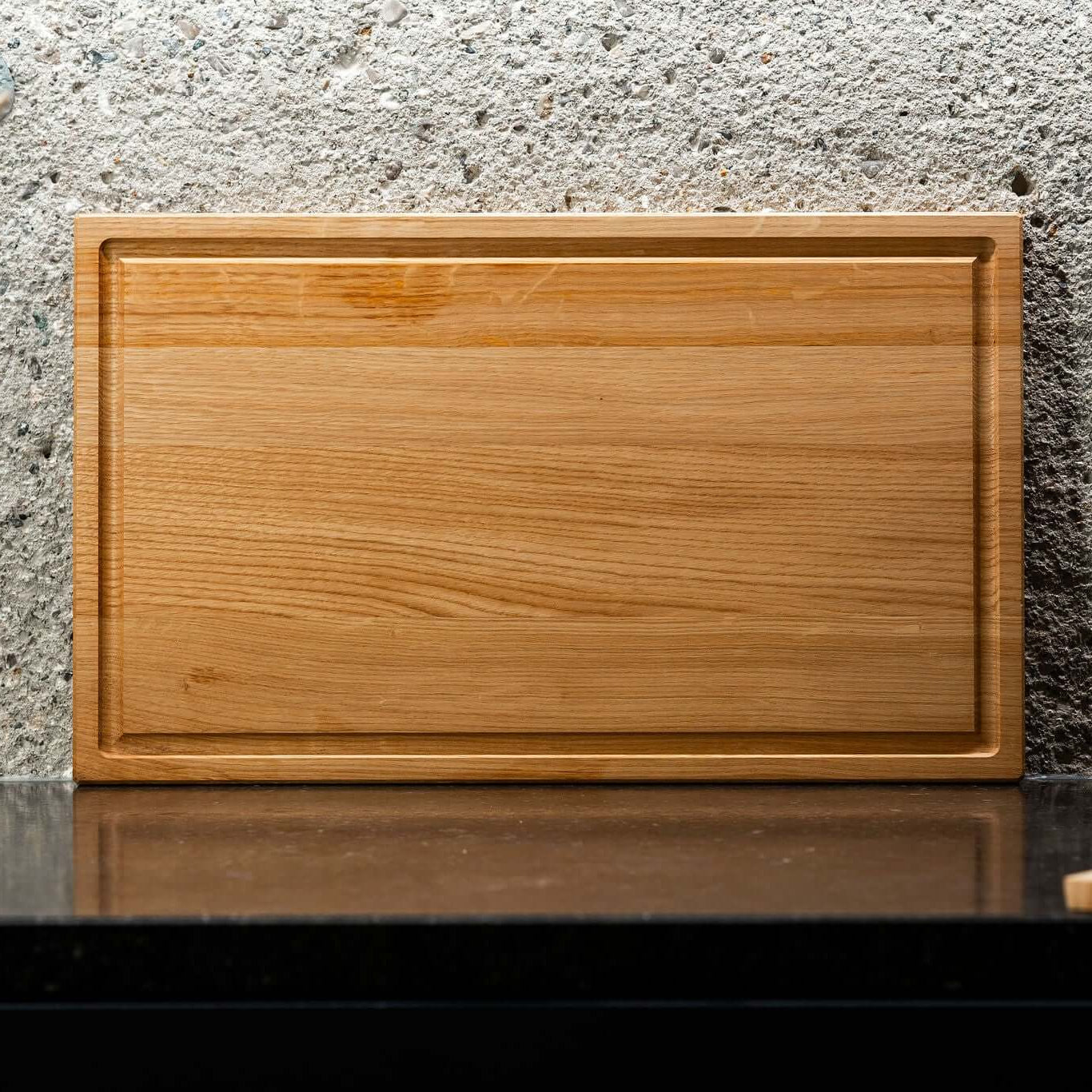 Eiche Längsholzschneidebrett auf einem schwarzen Tisch vor einer Betonwand, handgefertigt und FSC-zertifiziert.