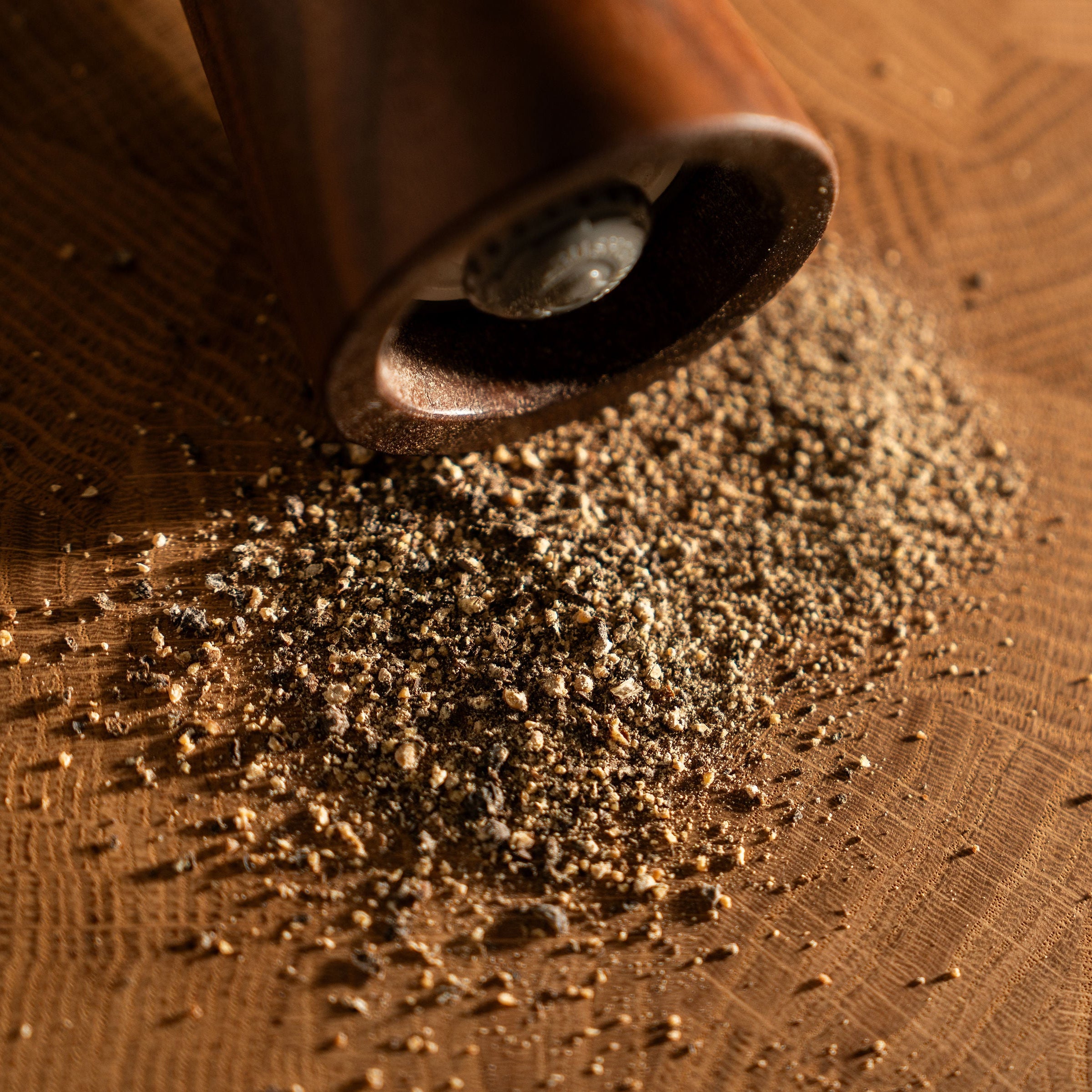 Handgefertigte Salzmühle Pfeffermühle mit frisch gemahlenem Pfeffer auf Holzunterlage.