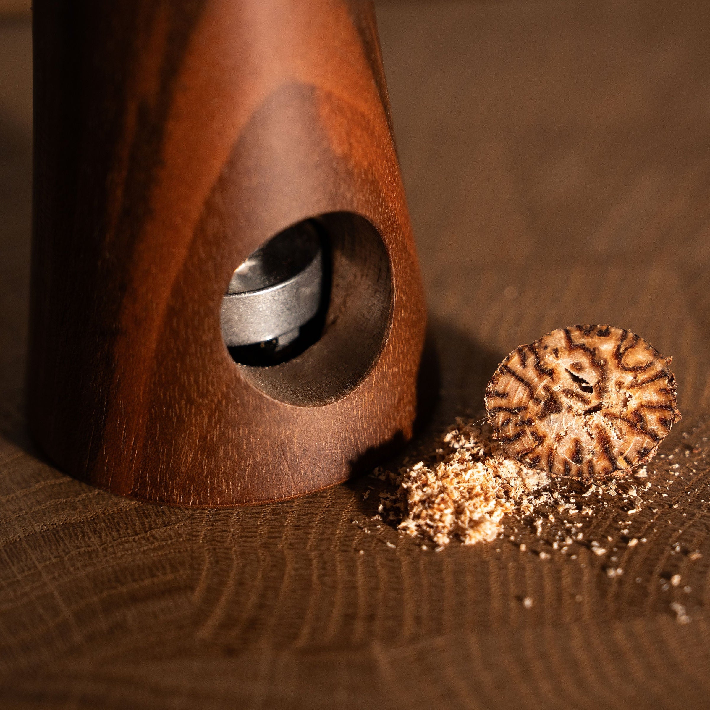 handgefertigte Muskatnussmühle aus Eiche und Nussbaum neben frisch gemahlener Muskatnuss auf Holzuntergrund